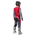 Alpinestars 2024 Supertech Dade Trikot, Motocross-Trikot, Iron Red Berry und Grau, Rückansicht eines Fahrers, mit einem roten Rückenteil, grauem Logo und grauen Ärmeln, getragen mit passender grau-roter Renn-Hose, weißen Stiefeln und einem schwarzen Helm, professionelle Offroad-Ausrüstung.