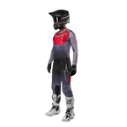 Motocross-Fahrer in kompletter Rennausrüstung, Alpinestars 2024 Supertech Dade Trikot in Iron Red Berry und Grau, passende graue Hose mit roten Akzenten, schwarzer Helm mit Goggles, weiß-schwarze Stiefel, schwarze Handschuhe, abgestimmtes Outfit für den Offroad-Rennsport