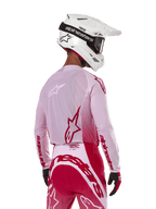 Motocross-Fahrer in der Rückansicht, trägt das Alpinestars 2024 Supertech Dade Jersey in Red Berry Lilac, mit atmungsaktiven Mesh-Panels und roten Alpinestars-Logos, kombiniert mit einer passenden rot-lilafarbenen Hose und einem weißen Alpinestars-Helm mit Brille, professionelle Offroad-Rennausrüstung