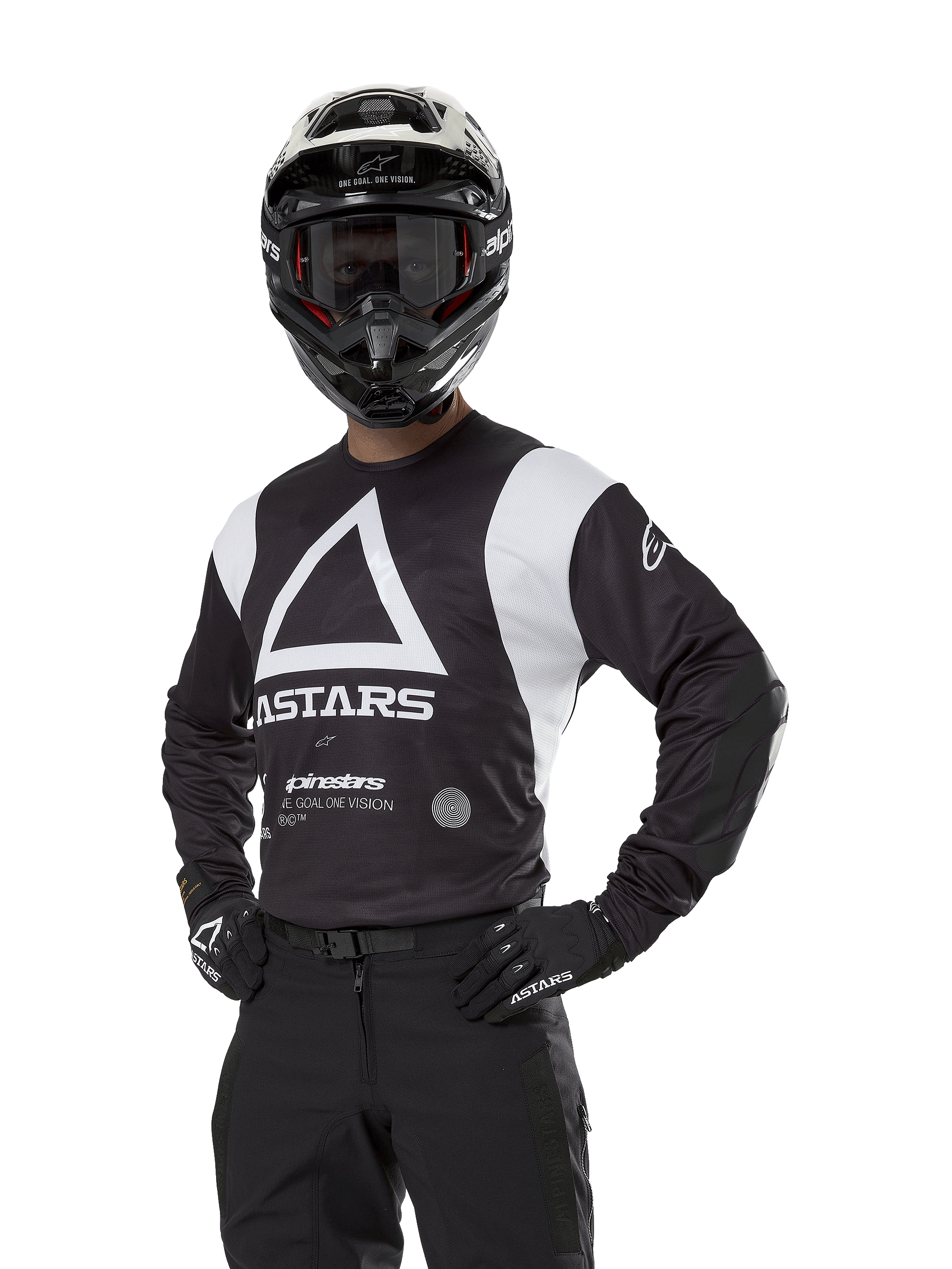 Maillot Alpinestars Techdura, maillot de motocross, noir et blanc, porté avec casque et gants assortis, pose les mains sur les hanches sur fond blanc, avec un grand logo A triangulaire et le marquage ASTARS