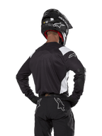 Maillot Alpinestars Techdura, noir avec accents blancs sur les épaules, vue de dos d'un pilote de motocross portant un pantalon et un casque noirs assortis, renforts aux coudes, équipement de course enduro et tout-terrain