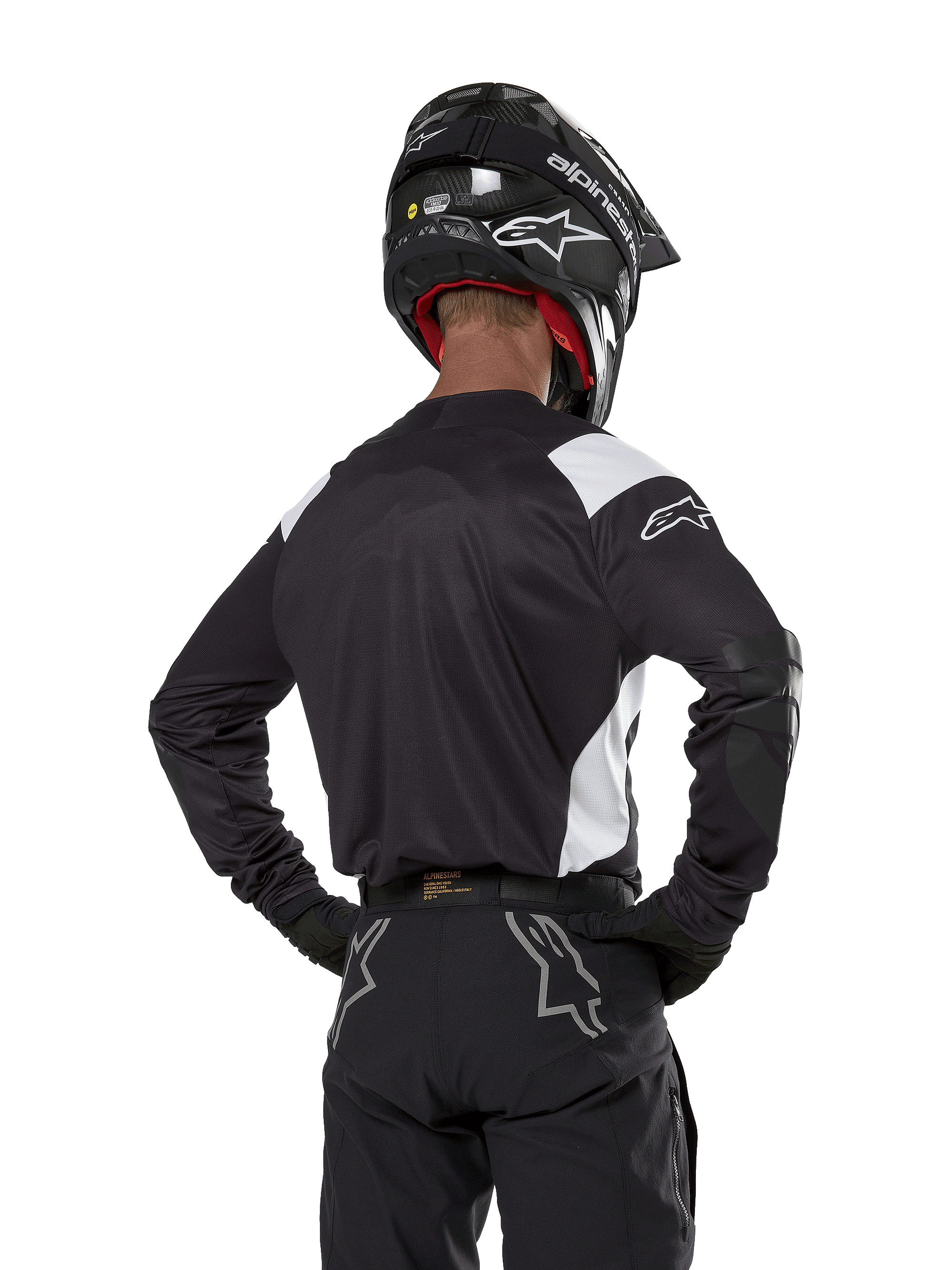 Maillot Alpinestars Techdura, noir avec accents blancs sur les épaules, vue de dos d'un pilote de motocross portant un pantalon et un casque noirs assortis, renforts aux coudes, équipement de course enduro et tout-terrain
