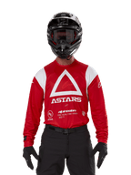 Alpinestars Techdura Jersey, felrood motorcross shirt met witte graphics, grote witte driehoek en ASTARS-logo op de borst, motorcrosser draagt zwarte helm, crossbril en zwarte uitrusting, gecoördineerde outfit voor enduro en off-road rijden