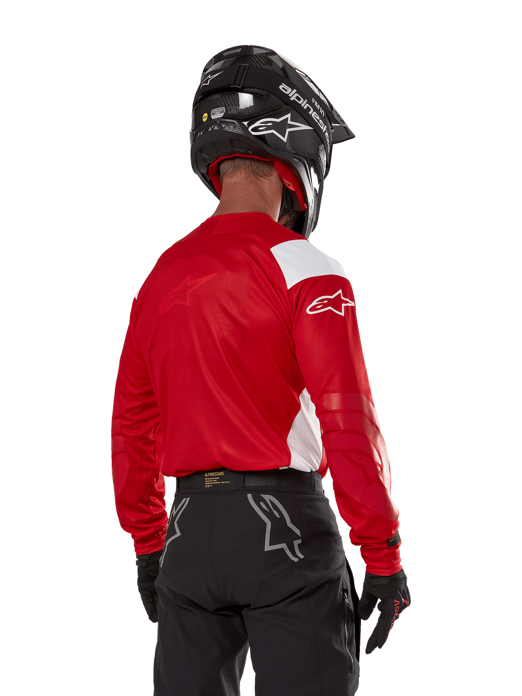 Alpinestars Techdura Jersey in Bright Red, motorcrosser van achteren gezien, helderrood shirt met witte panelen, zwarte off-road broek, zwarte helm en handschoenen, gecoördineerde uitrusting voor enduro- en motorcrossrijden