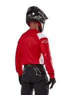Alpinestars Techdura Jersey in Bright Red, motorcrosser van achteren gezien, helderrood shirt met witte panelen, zwarte off-road broek, zwarte helm en handschoenen, gecoördineerde uitrusting voor enduro- en motorcrossrijden