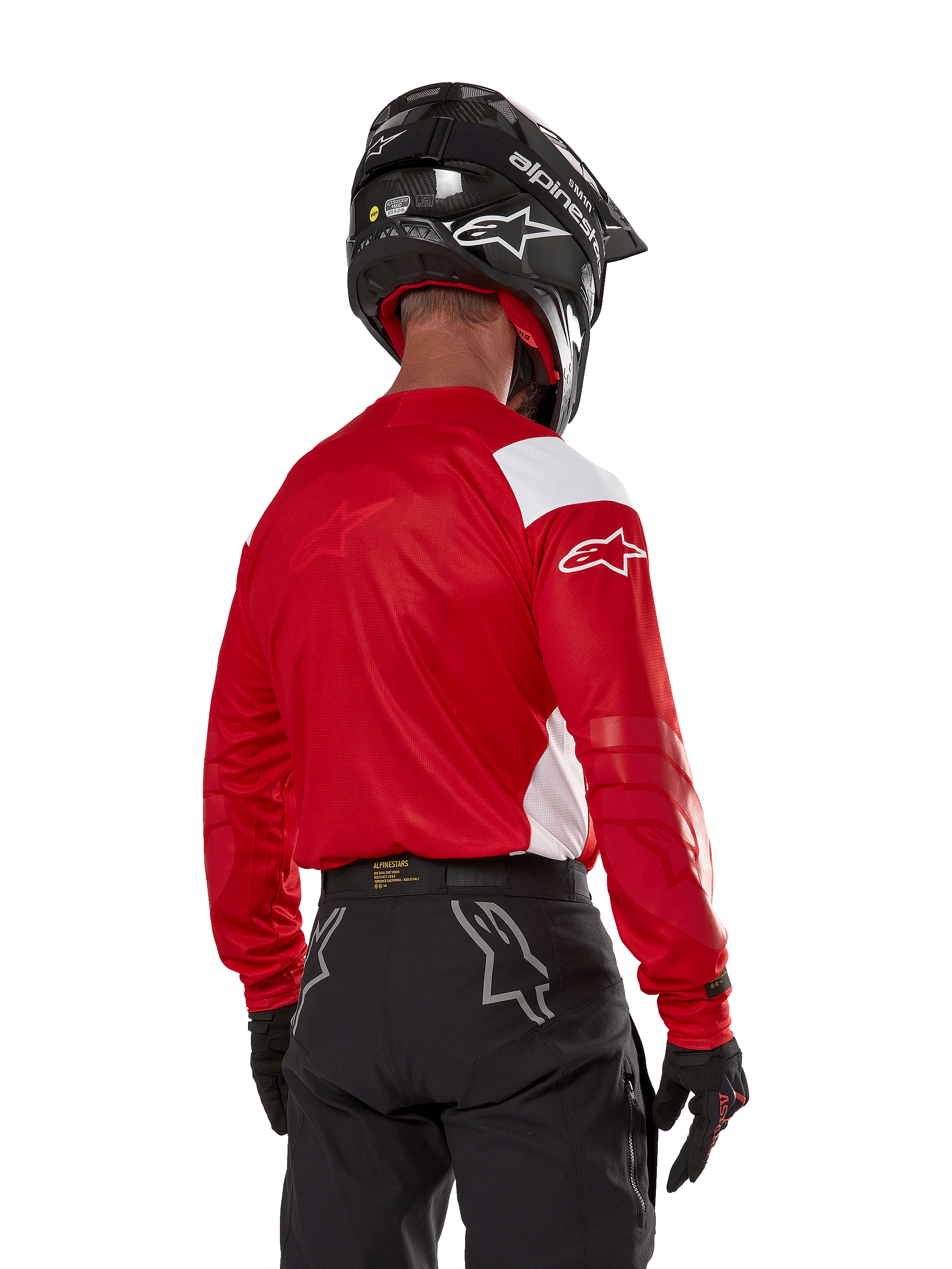 Alpinestars Techdura Jersey in Bright Red, motorcrosser van achteren gezien, helderrood shirt met witte panelen, zwarte off-road broek, zwarte helm en handschoenen, gecoördineerde uitrusting voor enduro- en motorcrossrijden