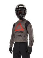 Alpinestars Techdura Jersey, Motocross Off-road Jersey, Falcon Brown with Red Triangle and black branding, worn with black pants, black and white helmet, and black gloves