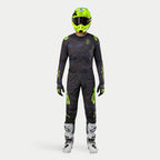 Pilote de motocross Alpinestars en tenue complète, Maillot Techstar Rantera 2024 noir, bleu marine et jaune fluo, pantalon assorti à motif abstrait, casque jaune fluo, bottes blanches et noires, équipement de course coordonné pour le tout-terrain