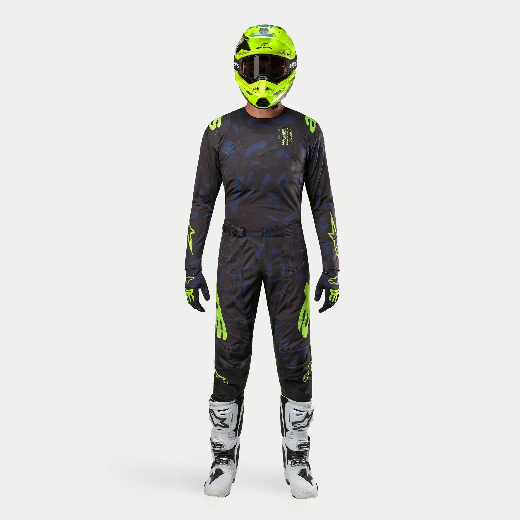 Pilote de motocross Alpinestars en tenue complète, Maillot Techstar Rantera 2024 noir, bleu marine et jaune fluo, pantalon assorti à motif abstrait, casque jaune fluo, bottes blanches et noires, équipement de course coordonné pour le tout-terrain