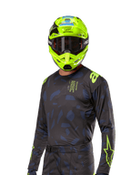 Alpinestars 2024 Techstar Rantera Jersey, maillot de motocross, noir et bleu marine avec motifs abstraits et accents jaune fluo, porté avec un casque jaune fluo assorti, design coupe performance pour la conduite tout-terrain
