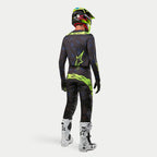 Maillot Alpinestars Techstar Rantera 2024, maillot de motocross, noir, bleu marine et jaune fluo, porté avec un pantalon assorti, des bottes blanches et noires et un casque jaune fluo, vue de dos en tenue de course tout-terrain complète