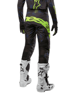 Pantalon Alpinestars 2024 Techstar Rantera, pantalon de motocross, noir, bleu marine et jaune fluo, vue arrière, avec logo jaune fluo audacieux et panneaux de ventilation en mesh, porté avec le maillot assorti et des bottes blanches, équipement durable pour le motocross et le tout-terrain