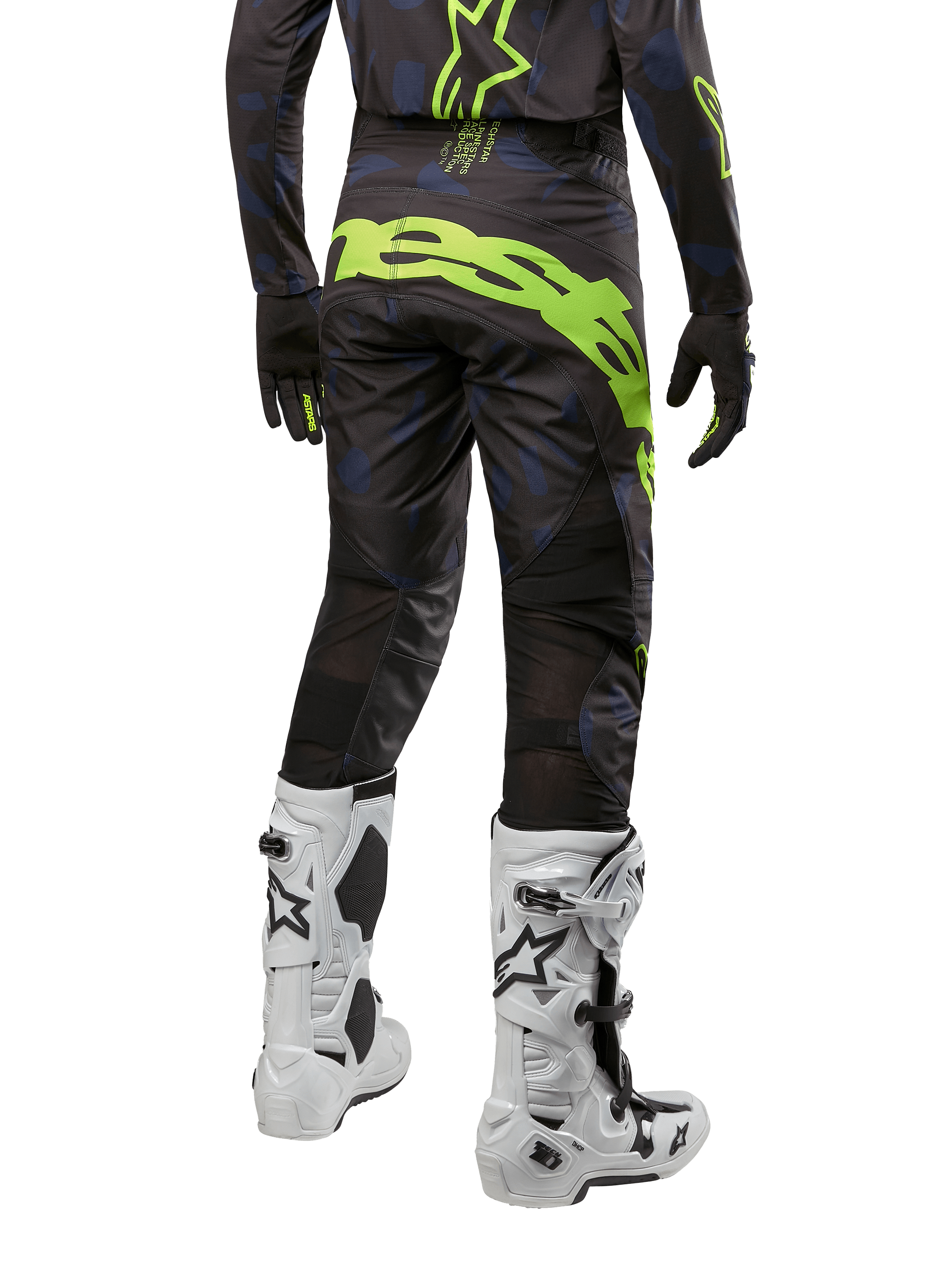 Pantalon Alpinestars 2024 Techstar Rantera, pantalon de motocross, noir, bleu marine et jaune fluo, vue arrière, avec logo jaune fluo audacieux et panneaux de ventilation en mesh, porté avec le maillot assorti et des bottes blanches, équipement durable pour le motocross et le tout-terrain