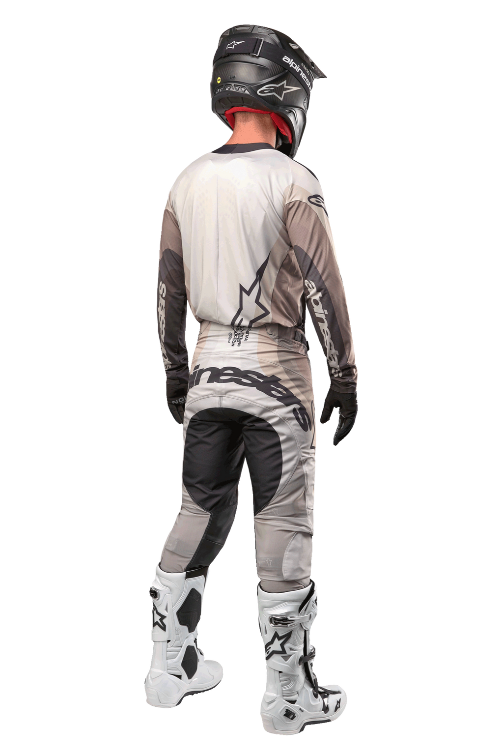 Pilote de motocross vu de dos portant le maillot Techstar Pneuma 2024 en Dark Sand Iron Dust Gray, pantalon de motocross assorti avec un logo imposant, casque noir et bottes de course blanches, équipement tout-terrain professionnel coordonné.