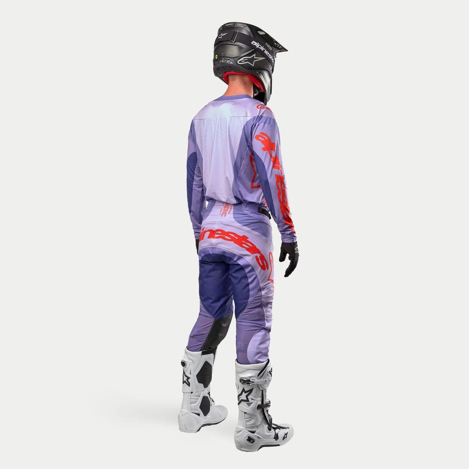 Tenue de motocross complète Alpinestars 2024 Techstar Ocuri, maillot et pantalon violets avec accents orange vif, casque noir, gants noirs et bottes de protection blanches, vue arrière de l'équipement de course coordonné.