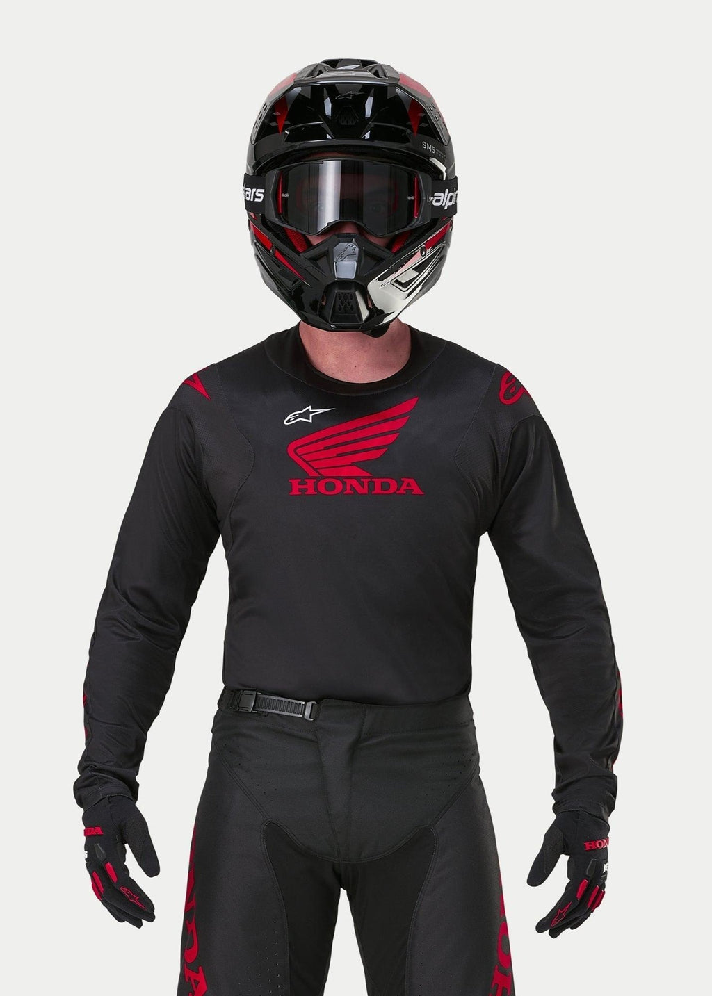 Motocross-Fahrer im Alpinestars Honda Racer Iconic Trikot in Schwarz und Rot, mit einem großen roten Honda-Flügel-Logo auf der Brust und weißem Astar-Logo, kombiniert mit einem passenden schwarzen Helm, einer Brille und Handschuhen für eine komplette Offroad-Rennausrüstung
