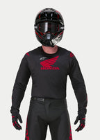 Motocross-Fahrer im Alpinestars Honda Racer Iconic Trikot in Schwarz und Rot, mit einem großen roten Honda-Flügel-Logo auf der Brust und weißem Astar-Logo, kombiniert mit einem passenden schwarzen Helm, einer Brille und Handschuhen für eine komplette Offroad-Rennausrüstung