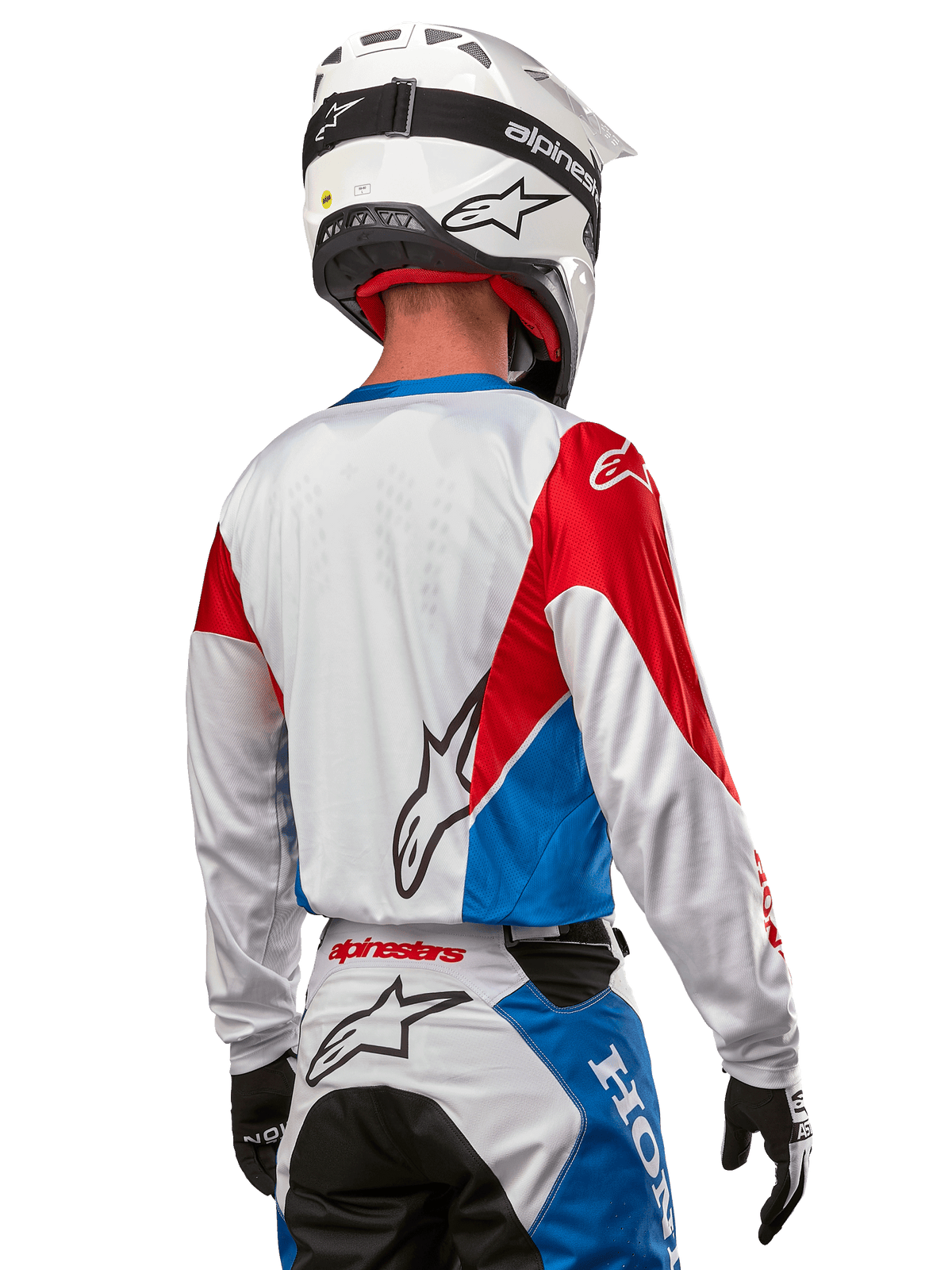 Motocross-Fahrer im Alpinestars Honda Racer Iconic Trikot, Rückansicht, Weiß mit leuchtend blauen und leuchtend roten Paneelen, markantes Alpinestars-Logo auf der Rückseite, kombiniert mit weißem Motocross-Helm und passender Rennhose.