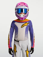 Alpinestars Jeugd Fluid Drag Jersey 2027, motocrossjersey voor kinderen in blauw en wit met goudkleurige accenten, ademend polyfabric voor off-road rijden, gedragen door een model met helm en handschoenen.