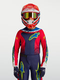 Maillot Fluid Drag Junior 2027 d'Alpinestars, maillot de motocross pour enfant, bleu marine et rouge avec accents jaunes, porté par un jeune pilote avec casque et gants.