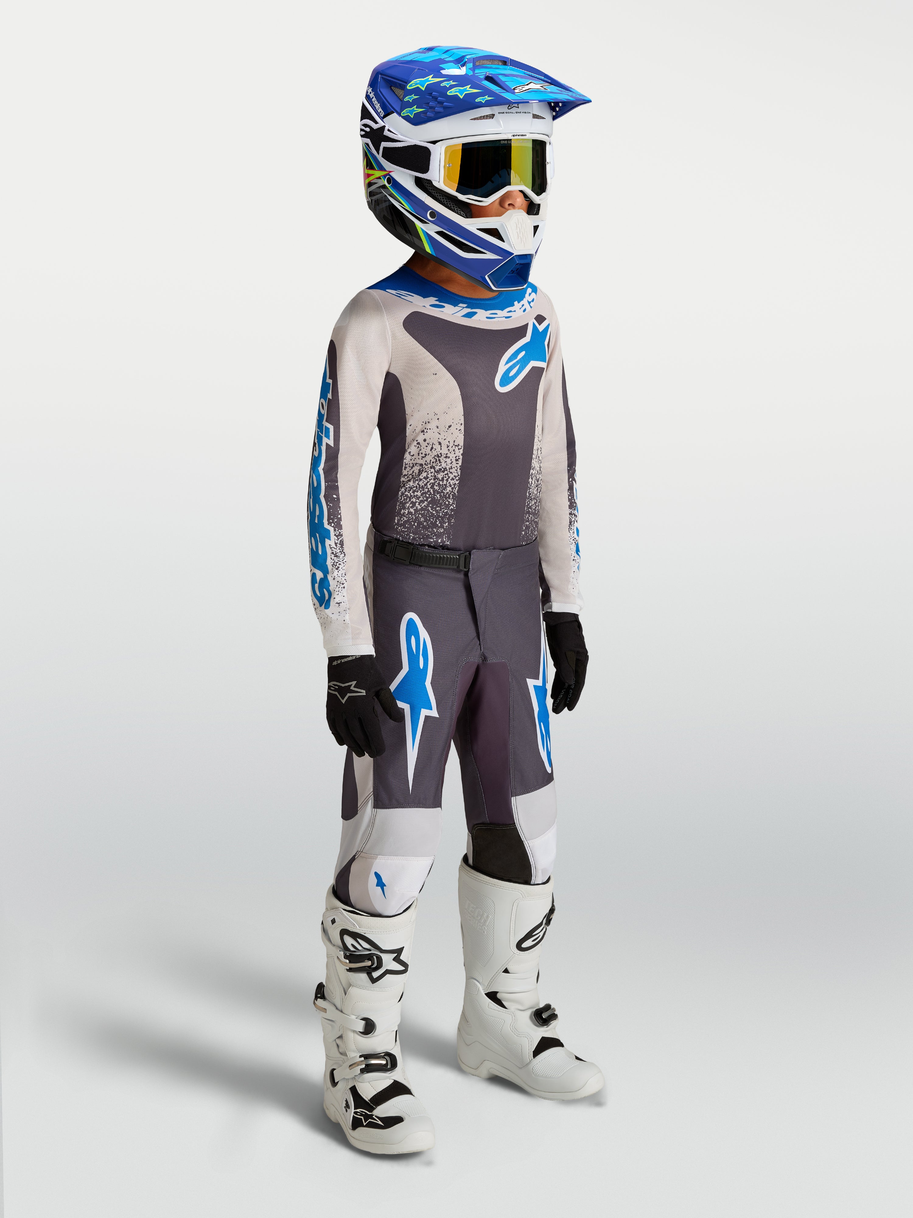 Alpinestars Jeugd Fluid Drag jersey en gear set 2027, grijze en blauwe motocrossuitrusting met witte motorlaarzen.