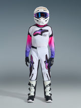 Youth motocross rider wearing complete racing gear, 2026 Youth Supertech Vista Jersey in white with pink and purple gradient sleeves, matching white and black pants with purple accents, white helmet with purple goggles, black and white boots, black gloves, coordinated high-performance outfit for off-road racing