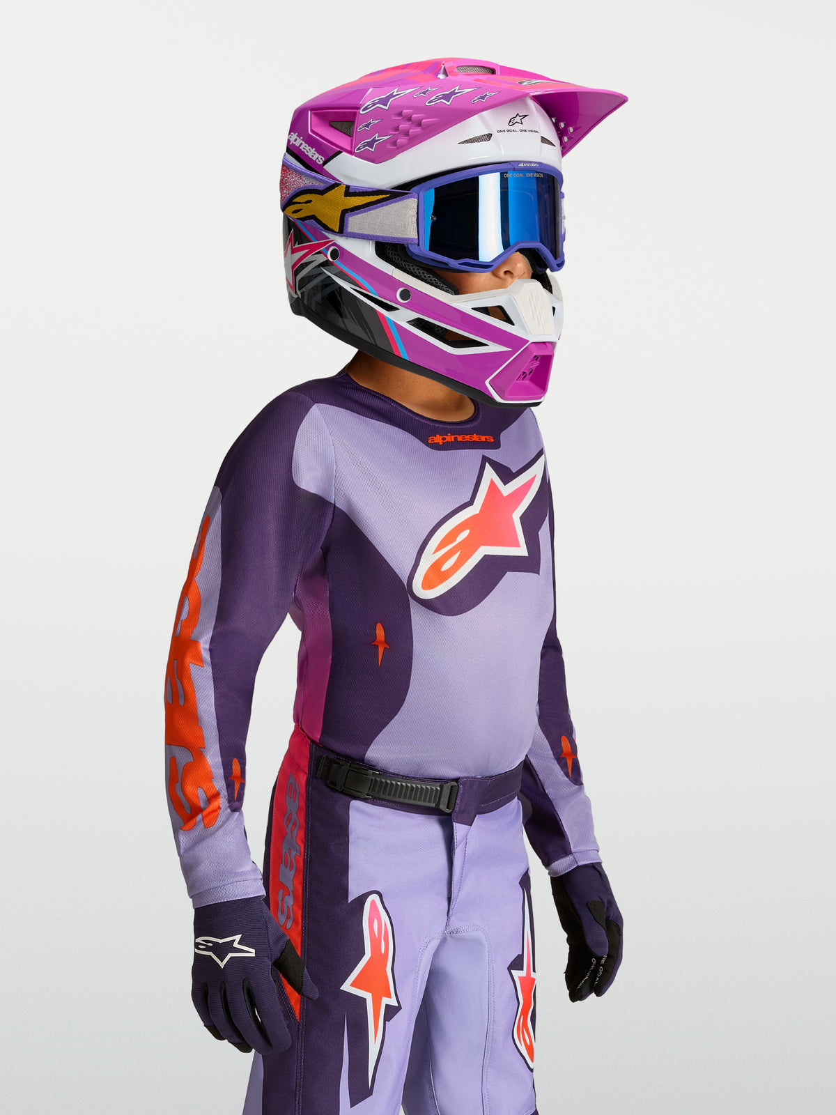 Alpinestars Fluid Hunt Jugend-Trikot 2027, Motocross-Ausrüstung für die Jugend, Lila und Violett, feuchtigkeitsableitende Textilkonstruktion, getragen von einem jungen Fahrer mit passendem Helm und Motocross-Handschuhen.