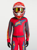 Maillot Alpinestars Fluid Hunt junior 2027, équipement de motocross rouge et gris, porté avec un casque de course.