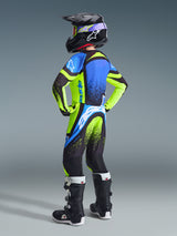 Alpinestars 2026 Jeugd Supertech Nomur jersey en broek, jeugd motocrossrijder van achteren gezien in volledige race-uitrusting, opvallend fluorgeel en donkerblauw met UCLA-blauwe accenten, bijpassende zwarte helm en laarzen, gecoördineerde pro-level off-road outfit
