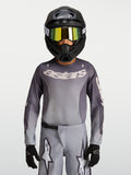 Alpinestars Jeugd Fluid Amber jersey, ademend motorcrossjersey in grijs en zand, gedragen door een jonge rijder met helm.