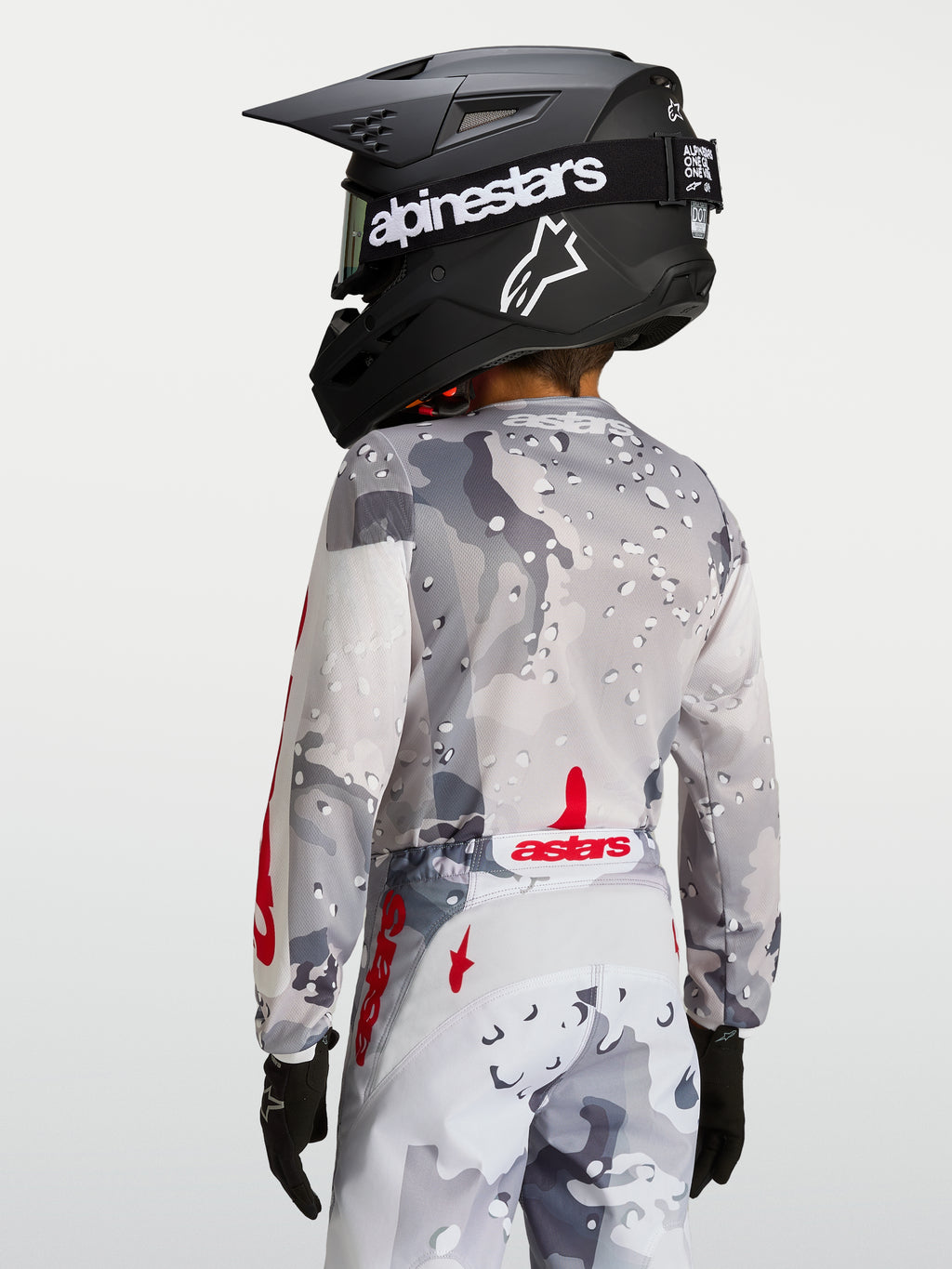 Alpinestars Maillot Fluid Lone Junior, haut de motocross pour enfant, gris camouflage et rouge, vue arrière montrant la coupe ergonomique et le bas du dos rallongé pour la conduite tout-terrain.
