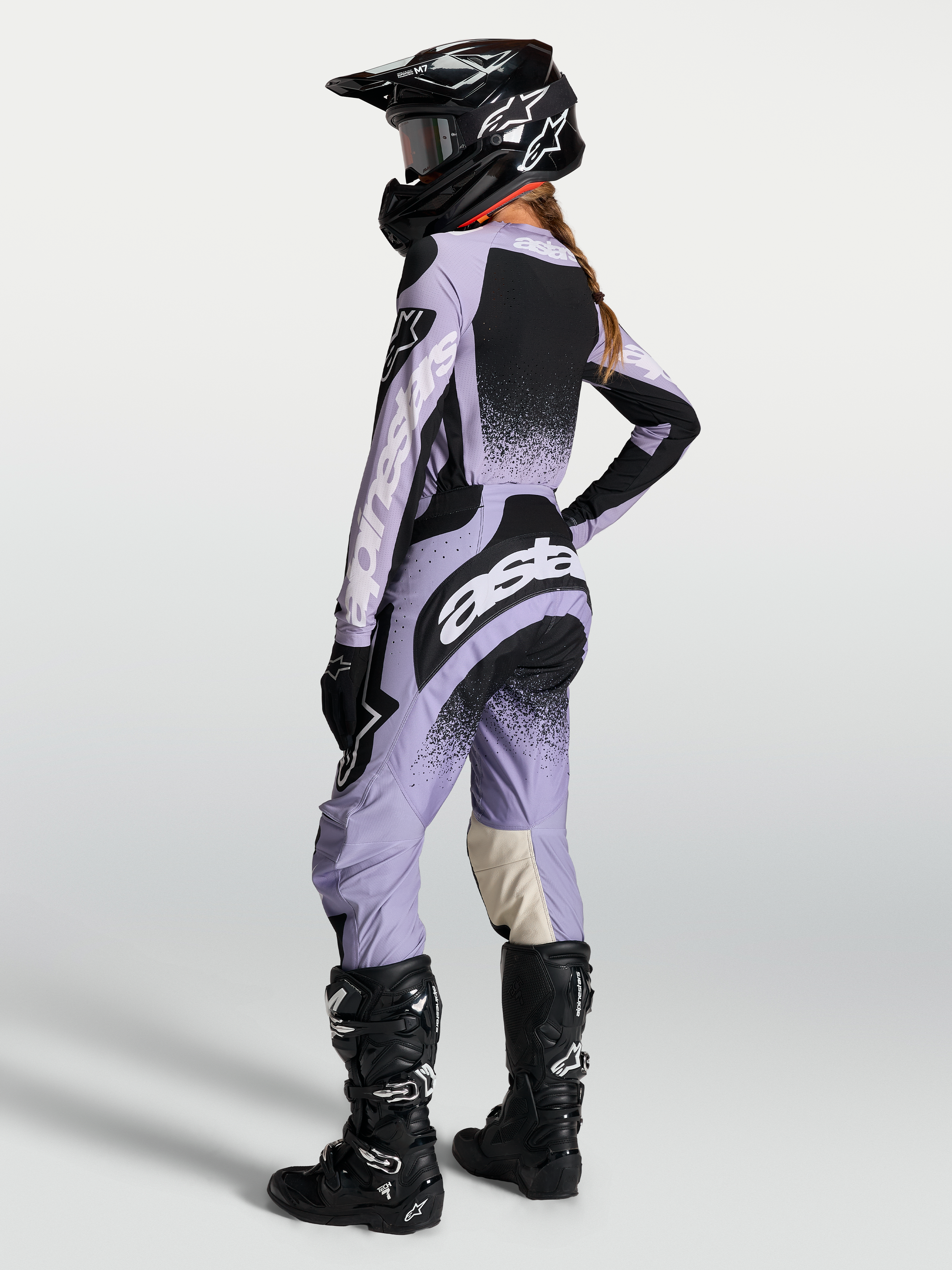 Alpinestars Stella Techstar Swan broek, dames-motorcrossbroek voor off-road racing, lichtpaars en zwart, ergonomische racepasvorm, gedragen door een model met bijpassende jersey en zwarte motorlaarzen.