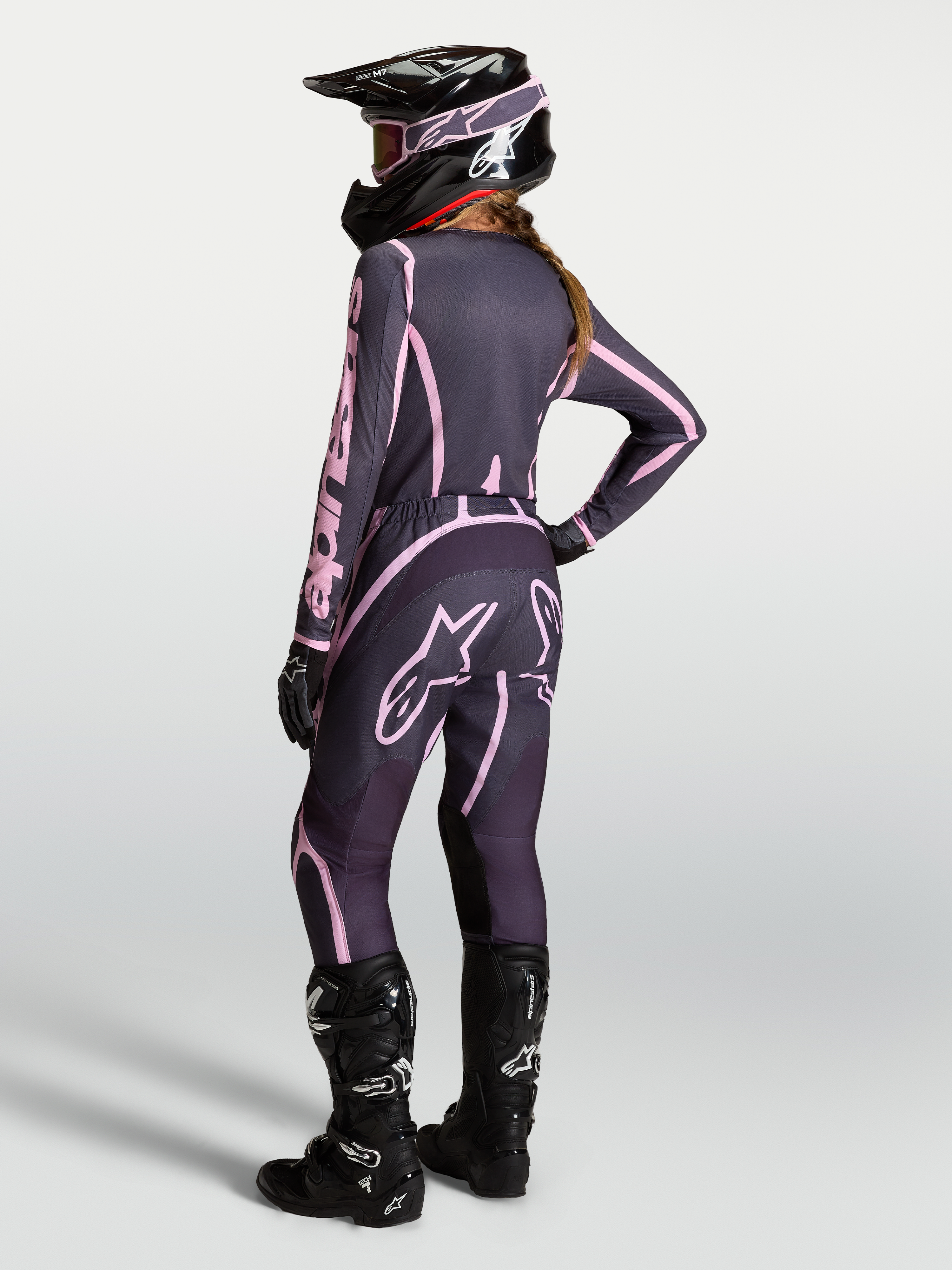 Alpinestars Stella Fluid Apex V2 jersey en kledingset voor dames, grijs en roze motocrossoutfit met zwarte motorlaarzen.