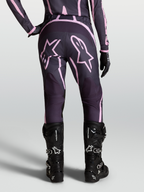 Alpinestars Stella Fluid Apex V2 broek, dames motorcrossbroek in grijs en roze met ster-graphics, gedragen met zwarte MX-laarzen en handschoenen.