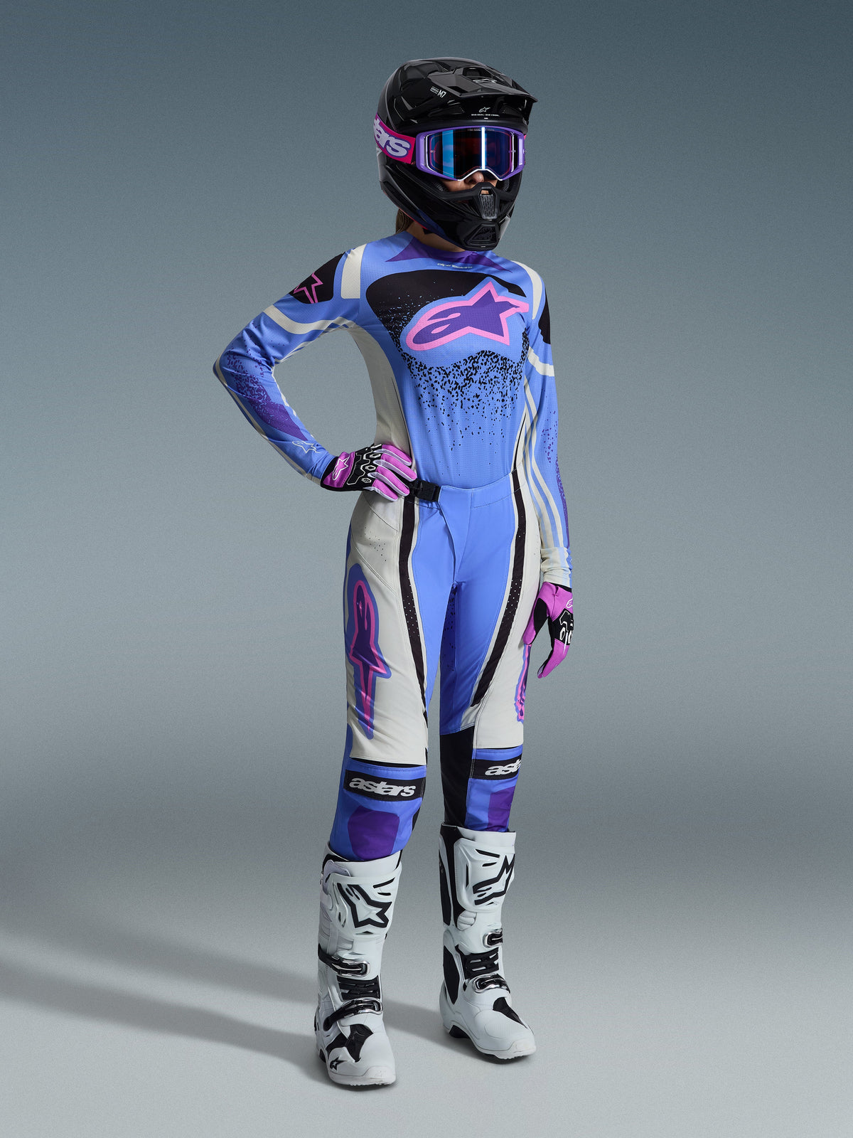 Alpinestars 2026 Stella Techstar Nomur Ausrüstungsset, Damen-Motocross-Ausrüstung, hellblaues Trikot mit pinkem Astar-Logo, passende Hose mit weiß-schwarzen Einsätzen, schwarzer Helm mit pink-lila Schutzbrille, pinke Handschuhe, weiße Motocross-Stiefel