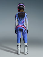 Vue arrière d'une pilote de motocross portant l'ensemble Alpinestars Stella Techstar Nomur 2026, maillot et pantalon bleus avec des accents roses et blancs, marquage rose vif à l'arrière du pantalon, avec des bottes de motocross blanches et un casque noir et rose coordonné.