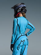 Ensemble Stella Fluid Apex 2026 d'Alpinestars, bleu clair et noir, vue de dos d'une pilote portant un maillot de motocross et un pantalon assorti, casque Alpinestars noir avec logo blanc, tenue technique de course tout-terrain pour femme
