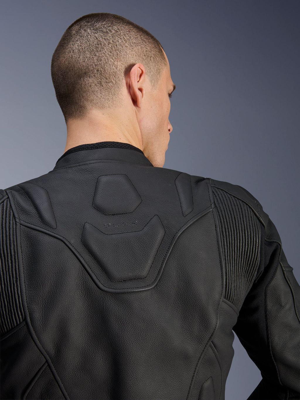 Alpinestars Dusk Lederjacke, Schwarz, Nahaufnahme des oberen Rückens und der Schultern mit dem geprägten DUSK-Logo auf einem gepolsterten Einsatz, Leder-Akkordeon-Stretcheinsätze, Konstruktion aus hochwertigem Rindsleder