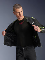 Männliches Model trägt die Alpinestars T-Sps Air V2 Jacke in Schwarz und Yellow Fluo, offen gezeigt, um die interne Mesh-Konstruktion und Taschen hervorzuheben, kombiniert mit einem schwarzen Alpinestars Base Layer und einer schwarzen Hose, urbaner Motorrad-Riding-Stil
