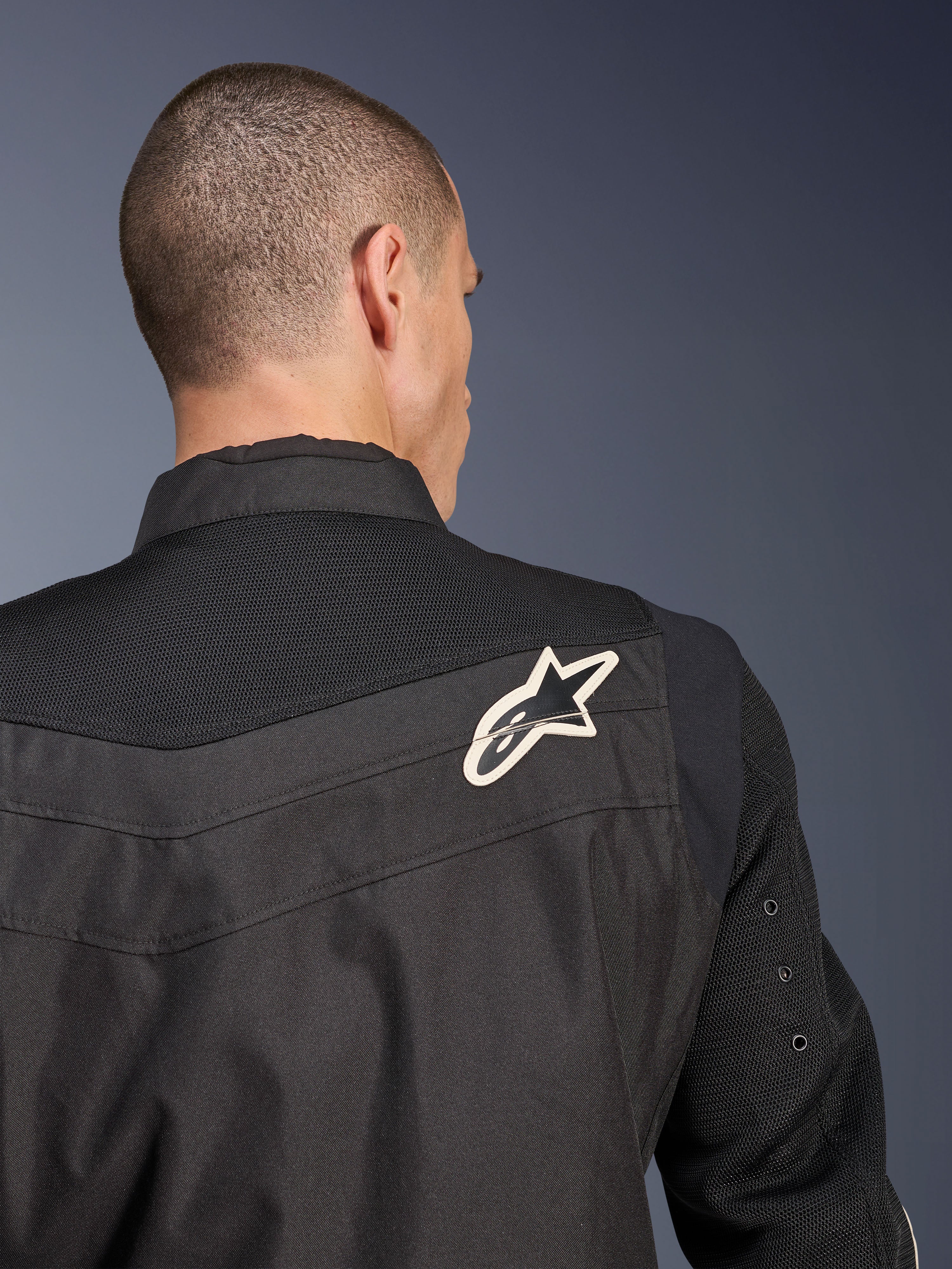 Blouson Alpinestars T-Dyno Air, blouson de moto en textile noir, vue arrière en gros plan soulignant l'empiècement et les manches en maille 3D respirante, arborant un logo étoile blanc et noir sur l'épaule droite.