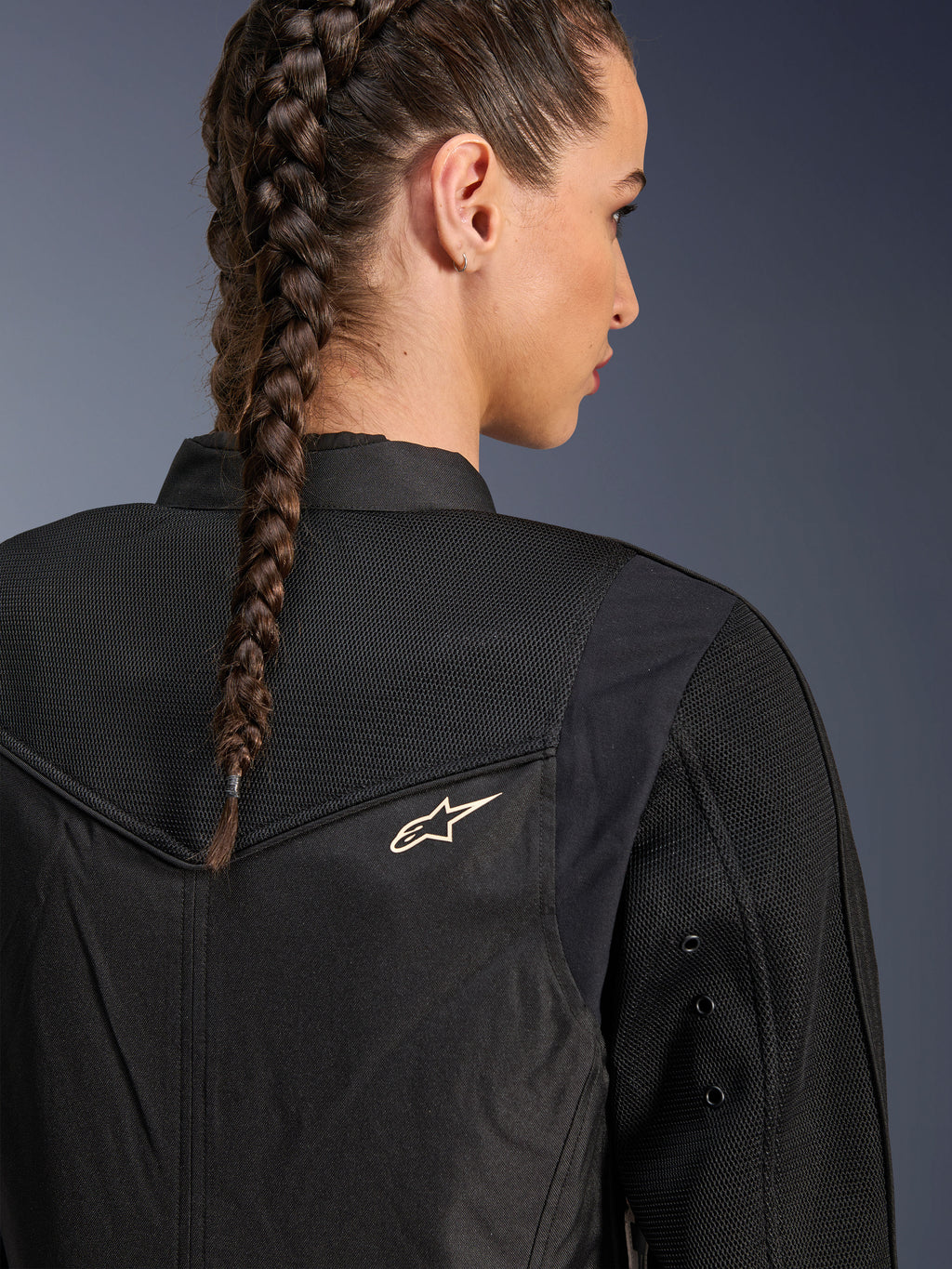 Alpinestars Stella T-Dyno Air Jacket, zwarte damesmotorjas, close-up achteraanzicht met 3D-meshpanelen op het juk en de bovenrug voor luchtstroom, voorzien van een klein wit sterlogo, gedragen door een model met gevlochten haar