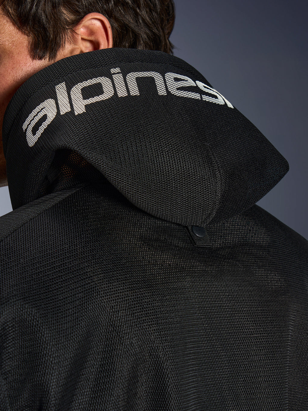 Alpinestars Chrome Superairflow Hoodie, noir, vue détaillée de la capuche en maille 3D avec marquage Alpinestars blanc sur le dessus, bouton-pression de stabilisation arrière, équipement de moto en textile ventilé pour chaleurs extrêmes