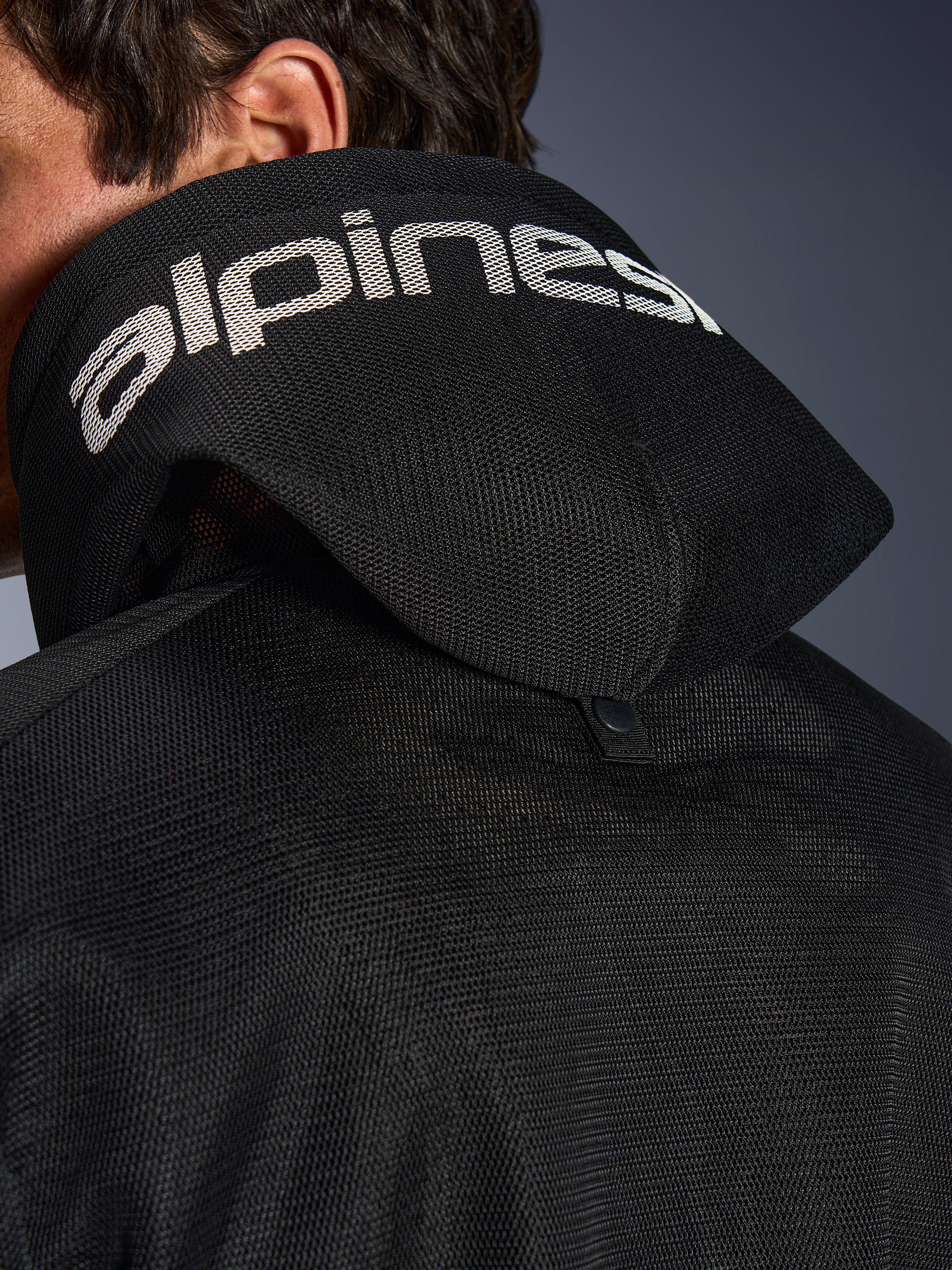 Alpinestars Chrome Superairflow Hoodie, noir, vue détaillée de la capuche en maille 3D avec marquage Alpinestars blanc sur le dessus, bouton-pression de stabilisation arrière, équipement de moto en textile ventilé pour chaleurs extrêmes