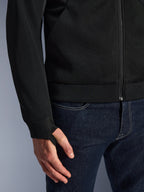 Alpinestars Chrome Superairflow Hoodie, noir, gros plan sur le tissu technique en maille 3D haute résistance, avec poignet en jersey côtelé extensible et boucle de rétention élastique pour le pouce, porté avec un jean bleu