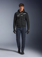 Motard portant le hoodie Alpinestars Chrome Superairflow noir et gris, associé à un jean bleu foncé, des gants de moto noirs et des chaussures noires. Le sweat à capuche présente un grand logo stylisé sur la poitrine et une texture en maille 3D pour une ventilation optimale par forte chaleur.