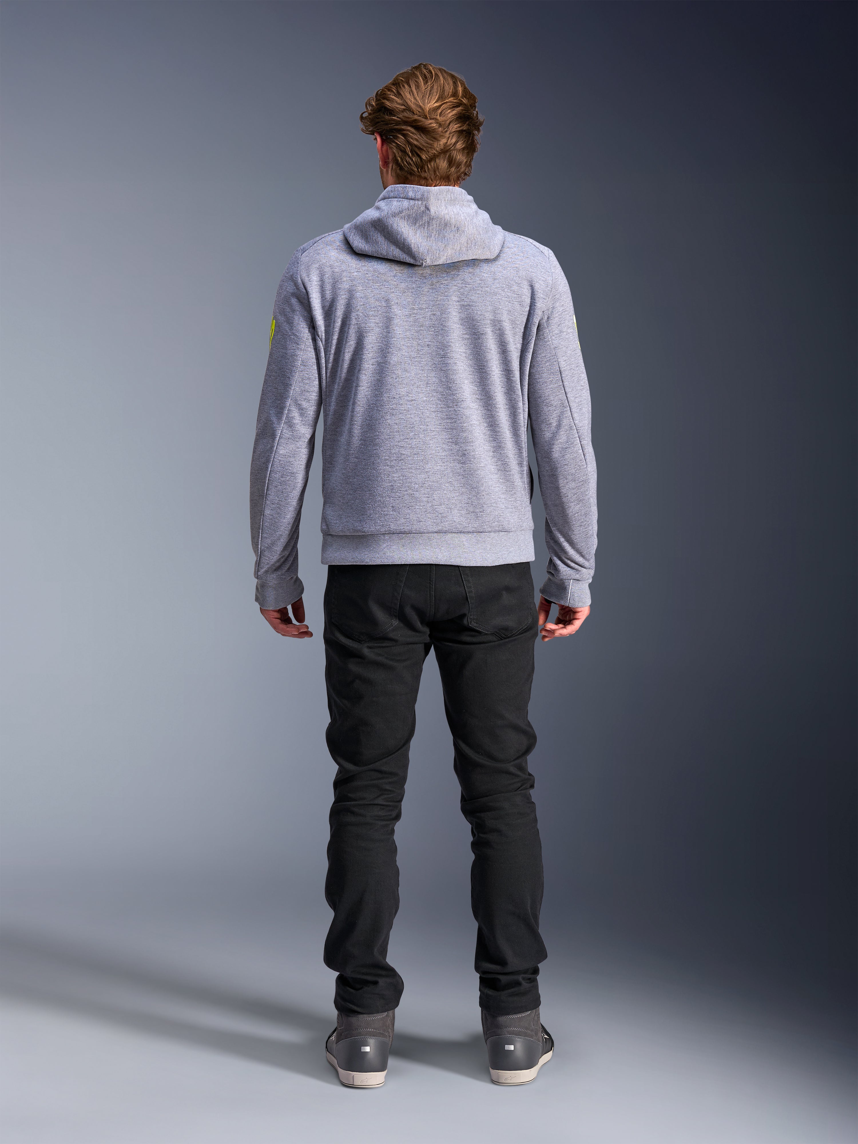 Alpinestars Chrome V2 Sport Hoodie, gris chiné jaune fluo, vue de dos d'un équipement de moto urbain, sweat à capuche en polaire technique porté avec un pantalon noir, doté d'accents jaune fluo sur les manches.