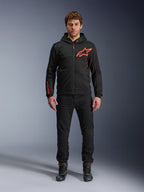 Alpinestars Chrome Air Sport Hoodie, Schwarz und Fluo-Rot, Urbane Motorradjacke mit Tech-Fleece-Konstruktion, mit großem rotem Astars-Logo auf der Brust und Schriftzug am Ärmel, getragen von einem Modell mit schwarzer Hose und Motorradschuhen