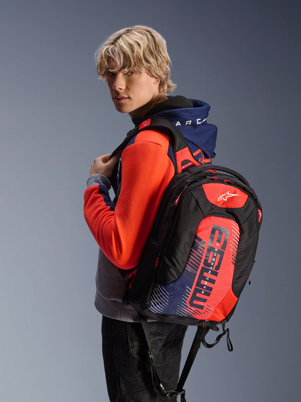 Sweat à capuche Alpinestars MM93 Chrome V2 Sport, bleu marine, gris chiné et rouge fluo, avec un sac à dos assorti de la marque MM93, vêtement de moto urbain décontracté, silhouette athlétique moderne
