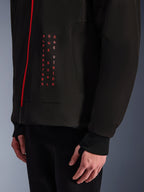Alpinestars Radium Tech Hoodie, urbane Motorradjacke, Schwarz und leuchtendes Rot, Nahaufnahme der Grafik mit vertikalem rotem Text „ALPINESTARS ONE GOAL ONE VISION“, roter Reißverschluss und geripptes Bündchen mit Daumenloch.
