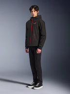 Alpinestars Radium Tech Hoodie, Schwarz-Hellrot, technischer Hoodie für urbanes Fahren mit rotem Frontreißverschluss und Logo auf der Brust, getragen von einem Modell mit schwarzer Hose und schwarzen Sneakern mit weißen Sohlen, Ganzkörper-Studioaufnahme